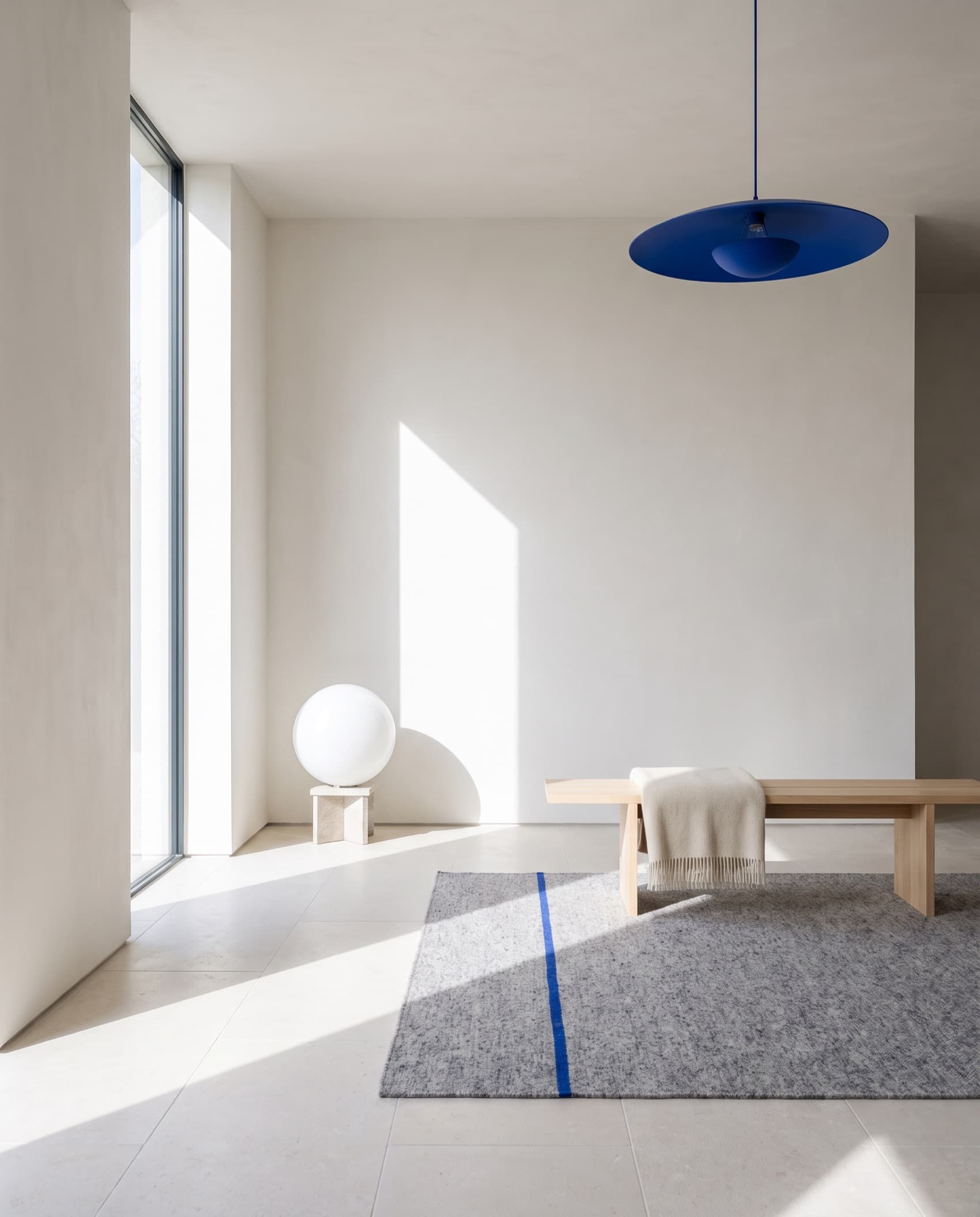 Séjour clair en plâtre blanc, suspension cobalt au-dessus d'un banc de chêne et tapis de laine grise